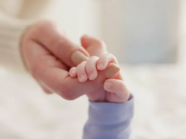 Baby und Erwachsener halten Händchen. 